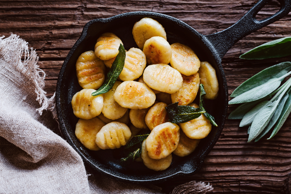 soft and pillowy vegan gnocchi in a black skillet with green leaves on top of it and a brown background