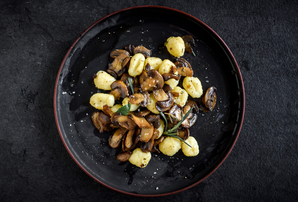 vegan mushroom gnocchi on a black plate with rosemary on a black counter