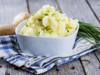 white bowl filled with the best vegan mashed potatoes with scallions and chives on top of a blue dish towel