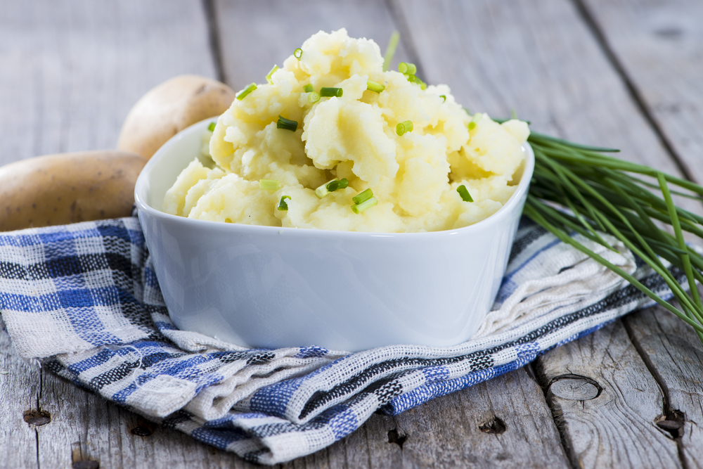 white bowl filled with the best vegan mashed potatoes with scallions and chives on top of a blue dish towel