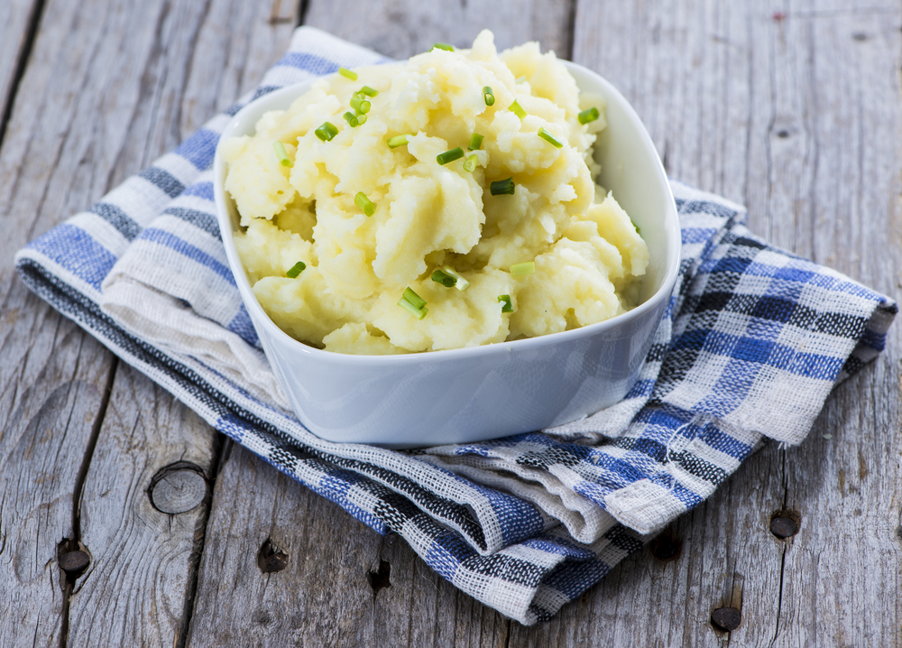 white bowl filled with creamy vegan mashed potatoes on a blue towel with green chives on top