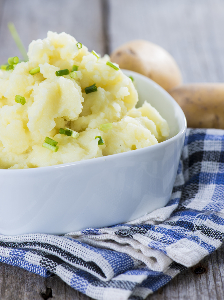 close up on a bowl of vegan mashed potatoes with green chives on top with a blue dish towel in the background