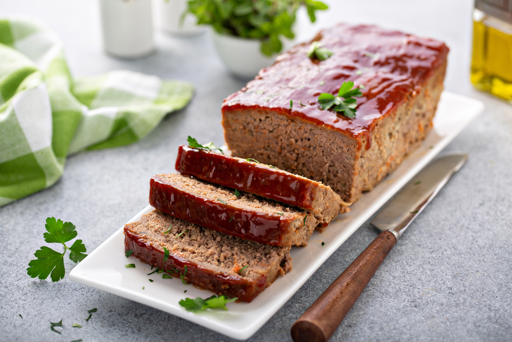 slices of a vegan meatloaf sitting on a white plate with a knife on the side and parsley on top of it. 