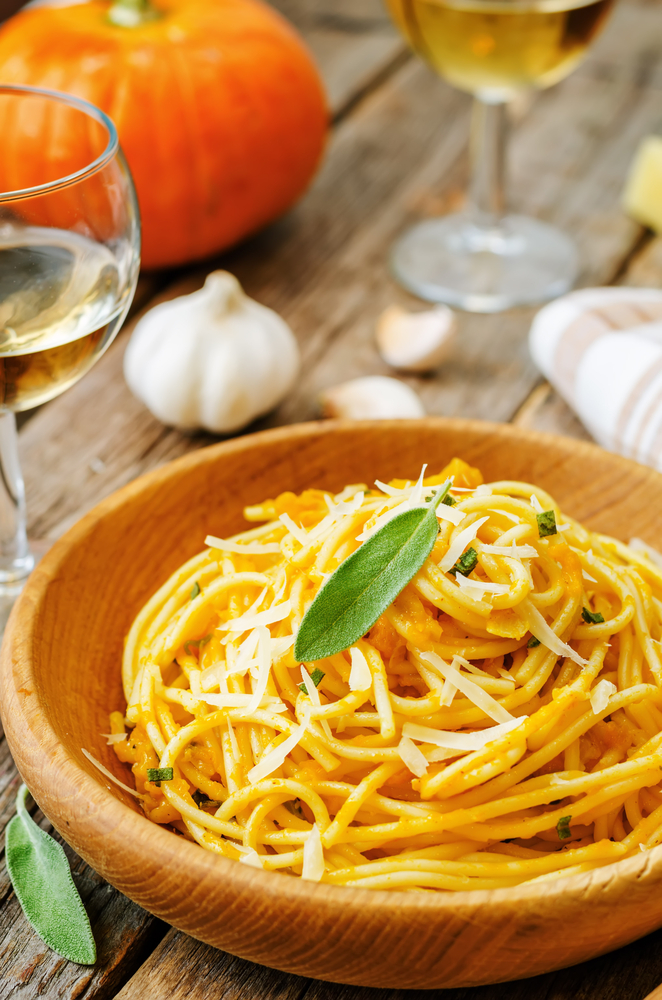pasta with pumpkin sauce in a brown bowl with shavings on it with wine in the background 