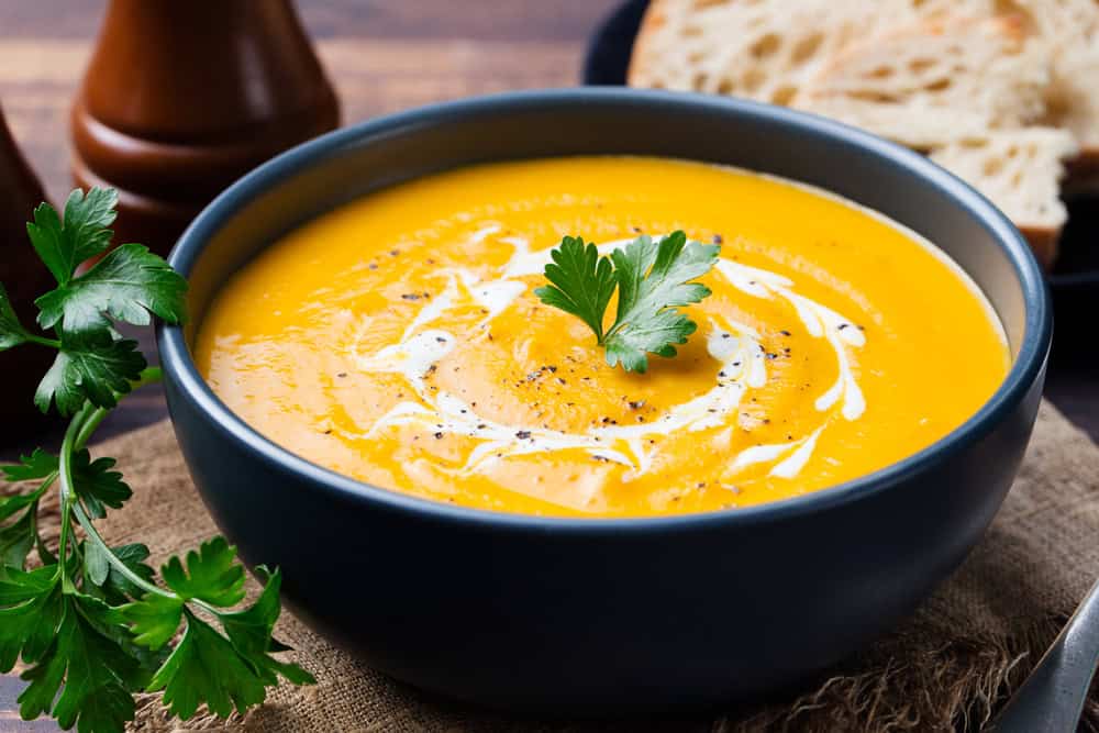 close up of vegan pumpkin soup in a black bowl with parsley on top of it