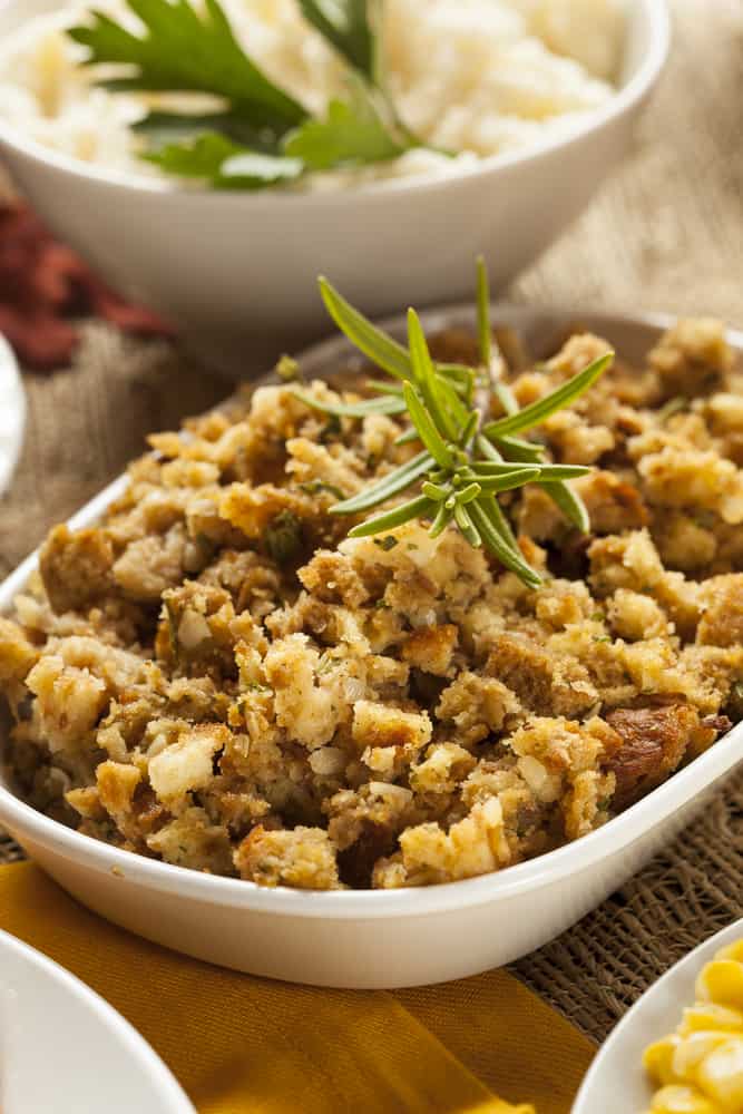 close up on vegetarian thanksgiving stuffing in a bowl with mashed potatoes in the background topped with a green parsley 