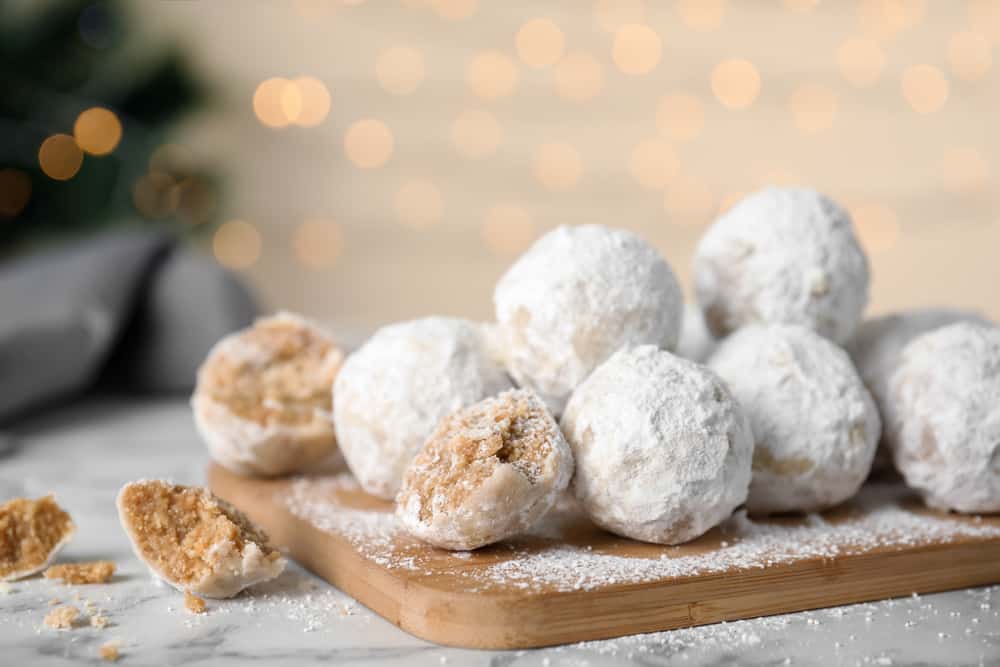 Wooden cutting board with pile of round butterball cookies covered in powdered sugar and some cut in half.