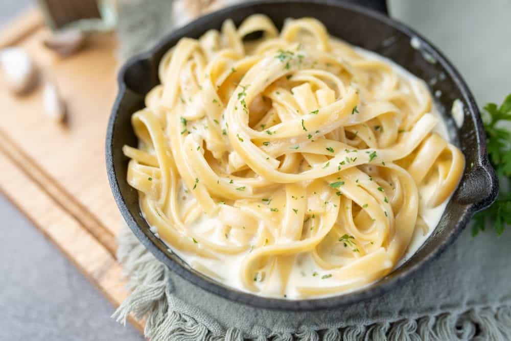 Vegan Alfredo Sauce with herbs on pasta in a cast iron pan .
