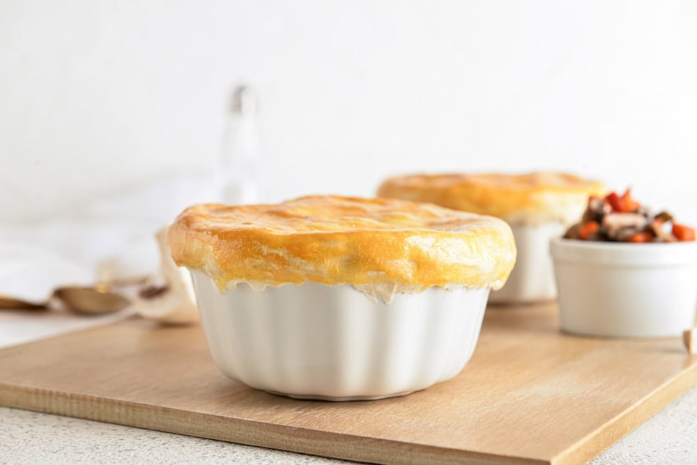 Pot pies in white ramekins on a wooden cutting board.