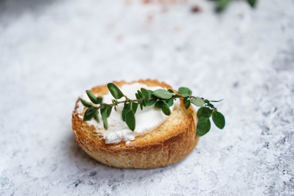 Round piece of bread with goat cheese spread and a garnish.