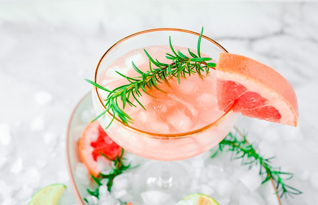 A Pink Grapefruit Cocktail with ice, sprig of rosemary and grapefruit garnish in a tub of ice.