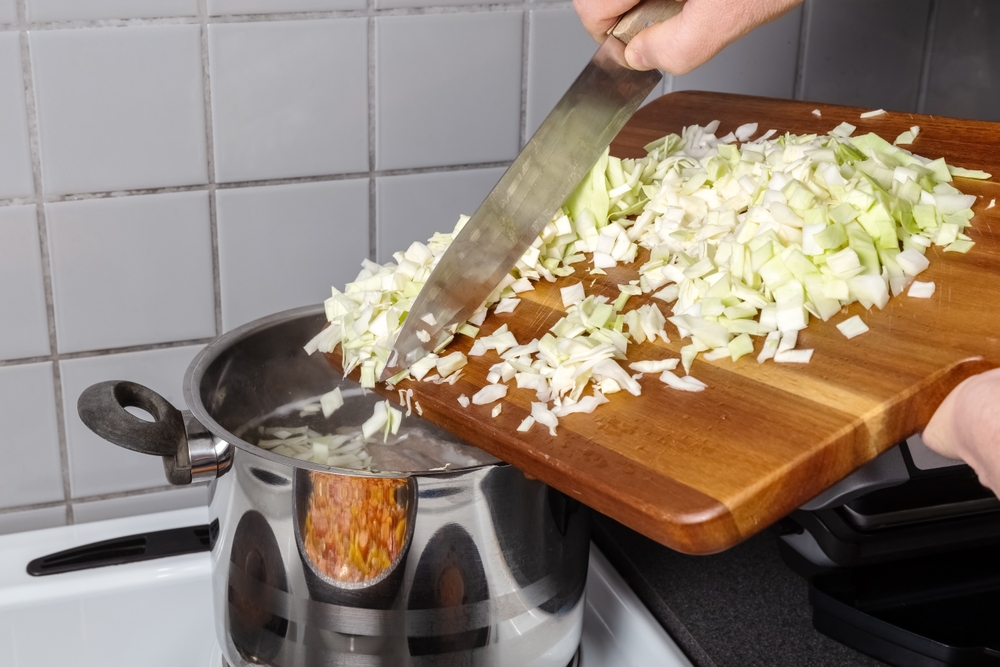 Person scrapping chopped cabbage into a pot on a stove.