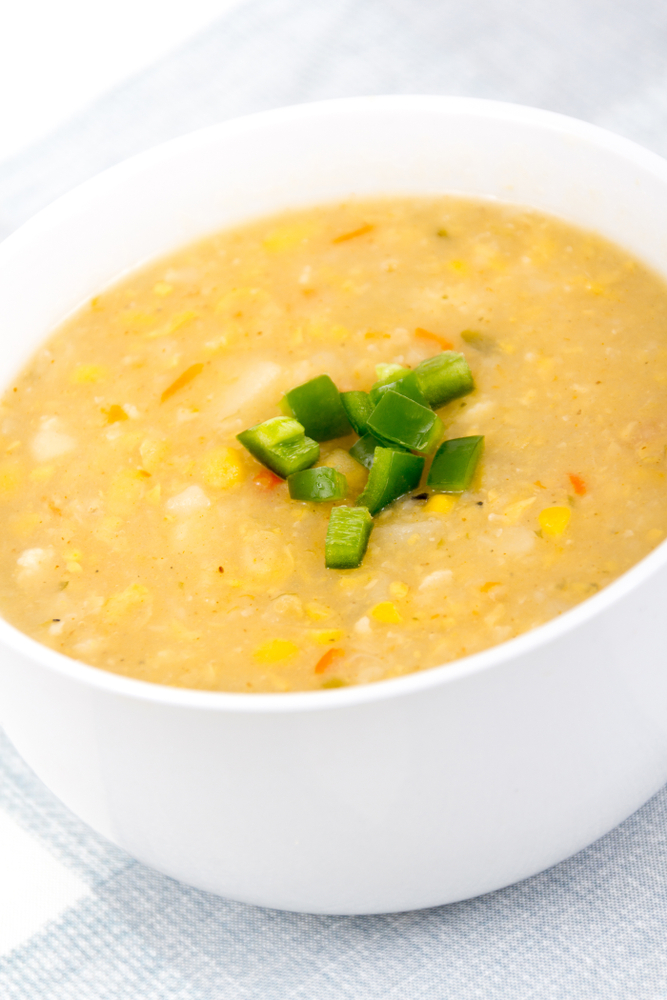 Close up of yellow corn soup with chopped green bell pepper on top in a white bowl.