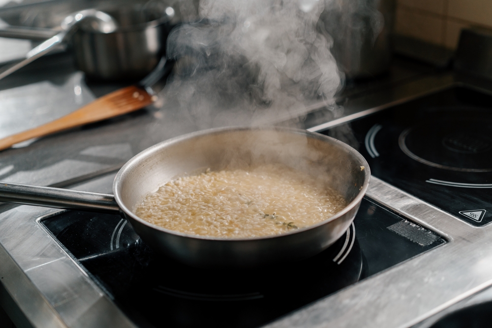 Risotto rice cooking in a steaming pan on a stove.