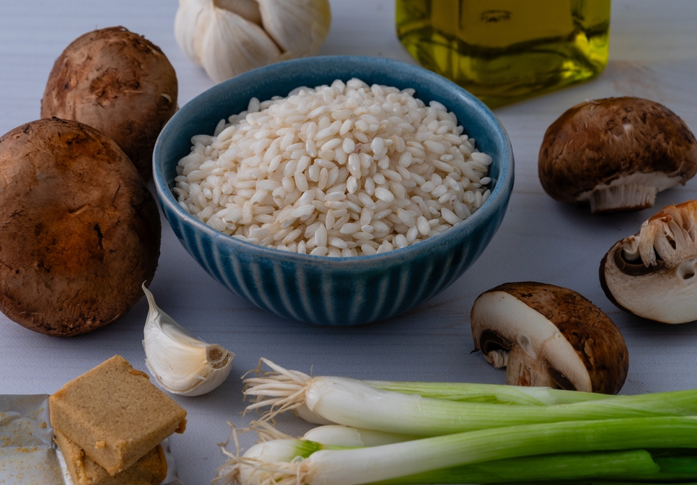 Blue bowl of risotto rice next to mushrooms and leeks.
