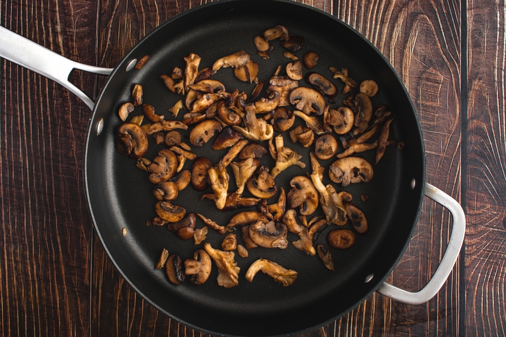 Sauteed mushrooms in a pan on a wooden background.