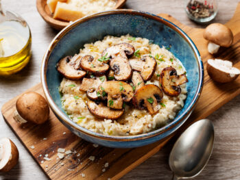 Wooden bowl of vegan risotto topped with sauteed mushrooms and seasonings.