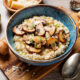Wooden bowl of vegan risotto topped with sauteed mushrooms and seasonings.