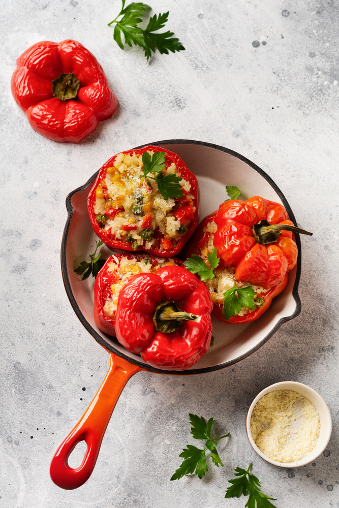 Flatlay of a ceramic pan holding three baked stuffed red bell peppers with cilantro.