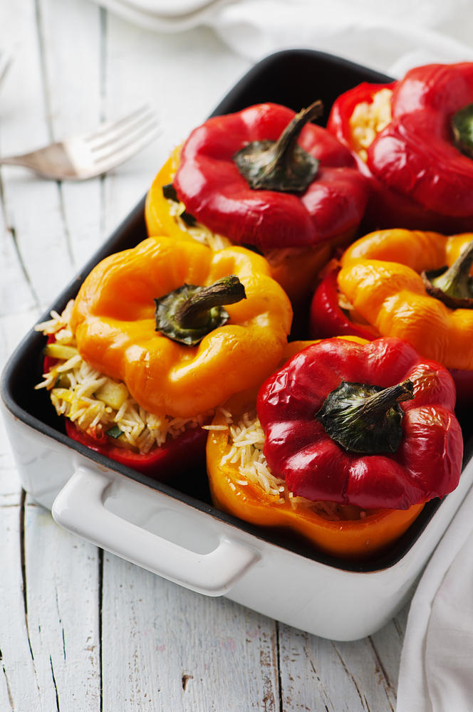 Baked red and yellow bell peppers stuffed with rice and vegetables in a ceramic baking dish.