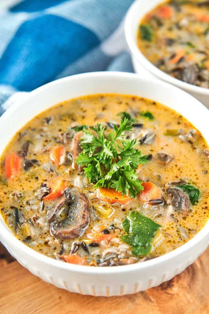 Two white bowls of colorful Vegan Wild Rice Soup with parsley garnish.