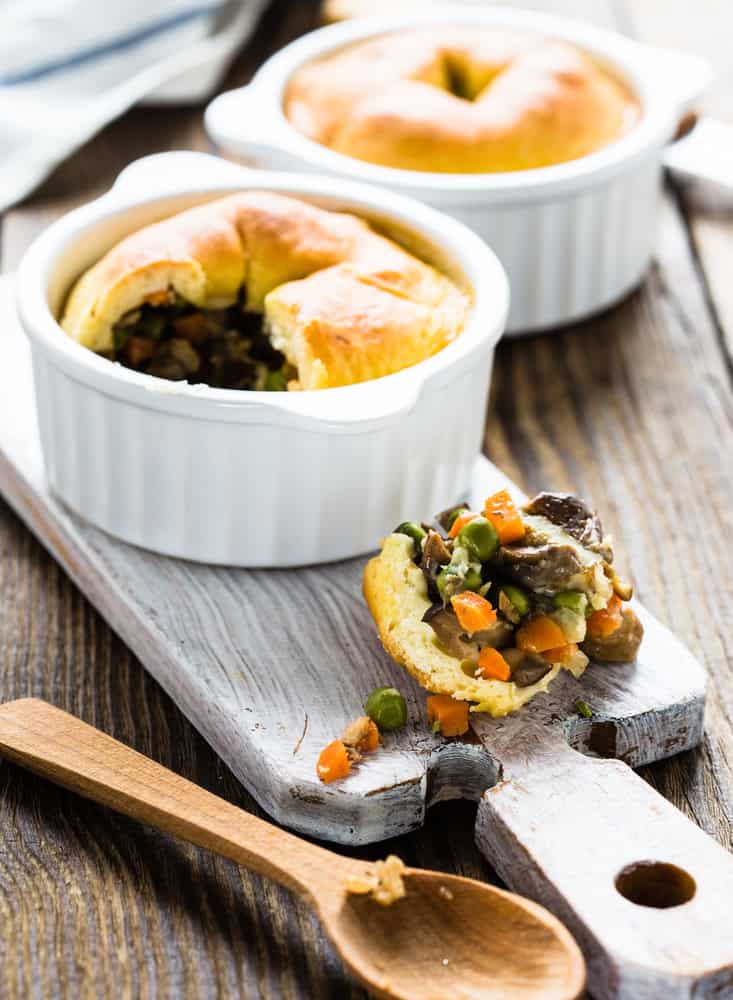 Individual pot pies in white ramekins on a wooden surface with a scooped out bite.