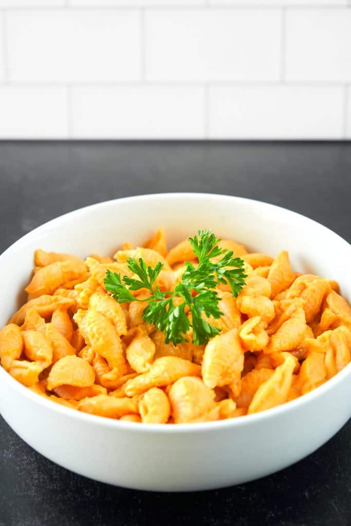 White bowl of creamy Vegan Butternut Squash Mac And Cheese with parsley garnish.