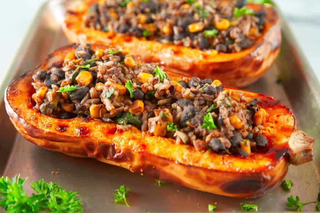 Two halves of a baked butternut squash filled with rice and vegetables on a baking sheet.