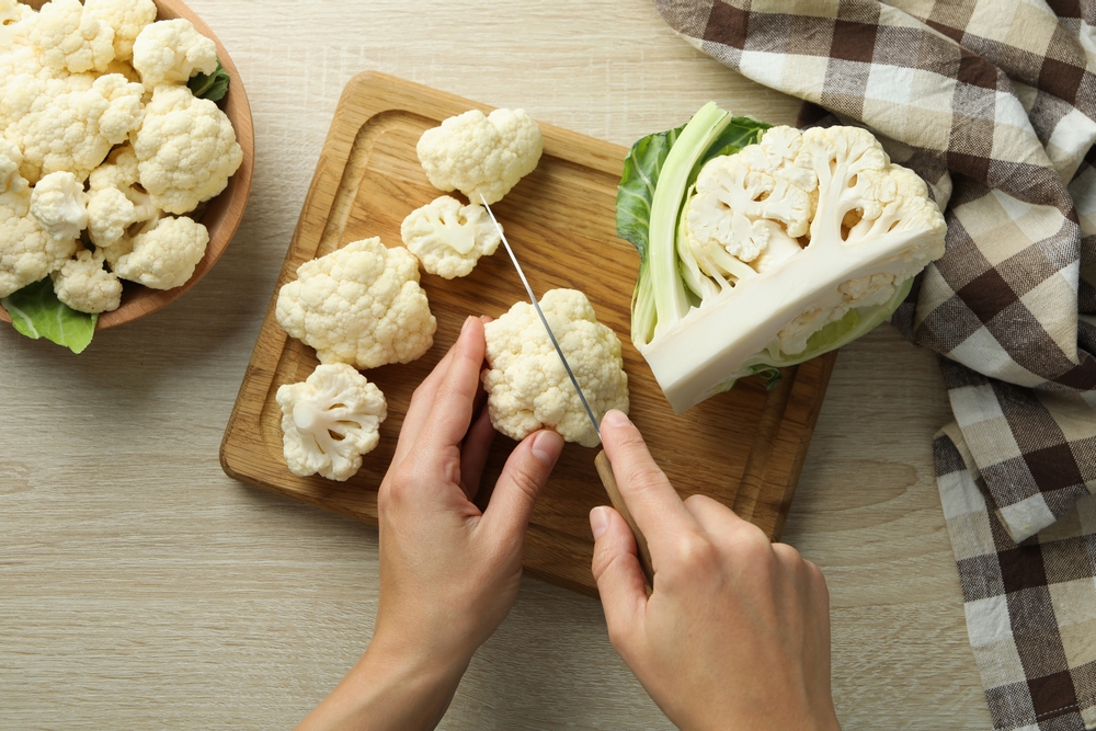 Female hands cut cauliflower on wooden board