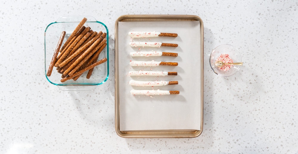 Flat lay. Homemade candy cane chocolate-covered pretzel rods are drying on a baking sheet lined with parchment paper.