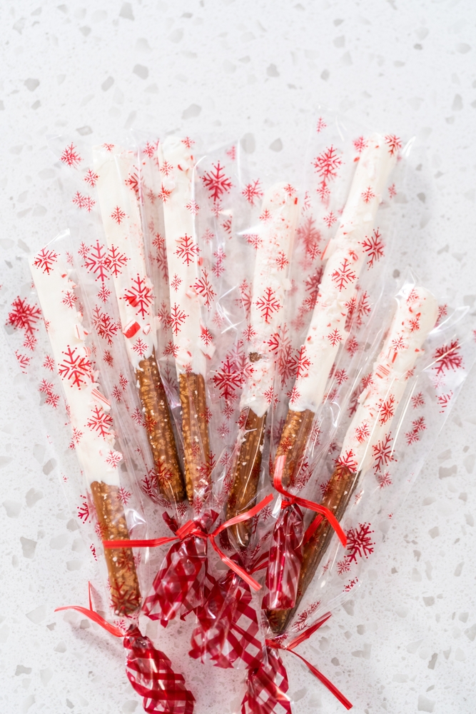 Packaging homemade candy cane chocolate-covered pretzel rods into clear plastic bags for Christmas gifts.