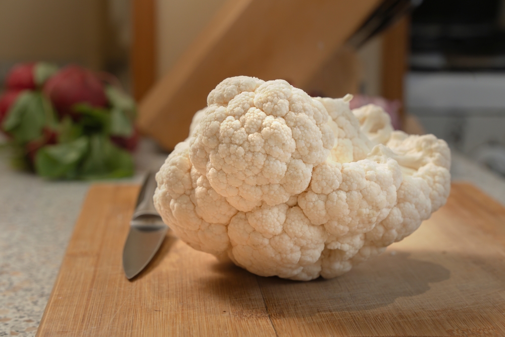 Whole head of cauliflower lies on a kitchen cutting board. Close-up