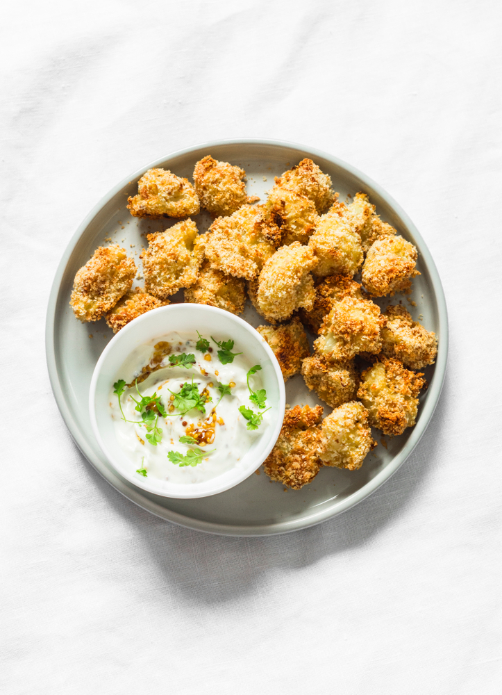 Baked crispy parmesan bread crumbs cauliflower bites with yogurt sauce on lightl background, top view        