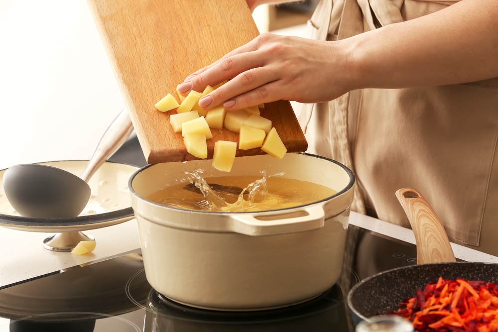 Woman adding potato to cooking pot in kitchen.