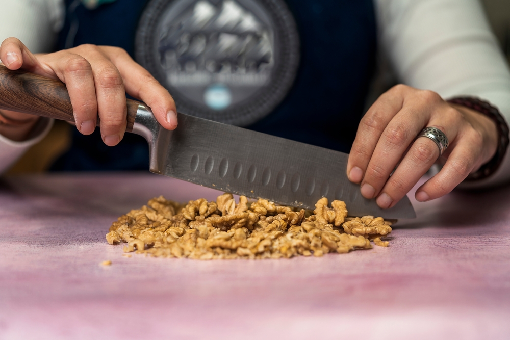 Unrecognizable person using a knife to cut walnuts into small pieces to decorate homemade argentine alfajores. Concept of regional, traditional food.