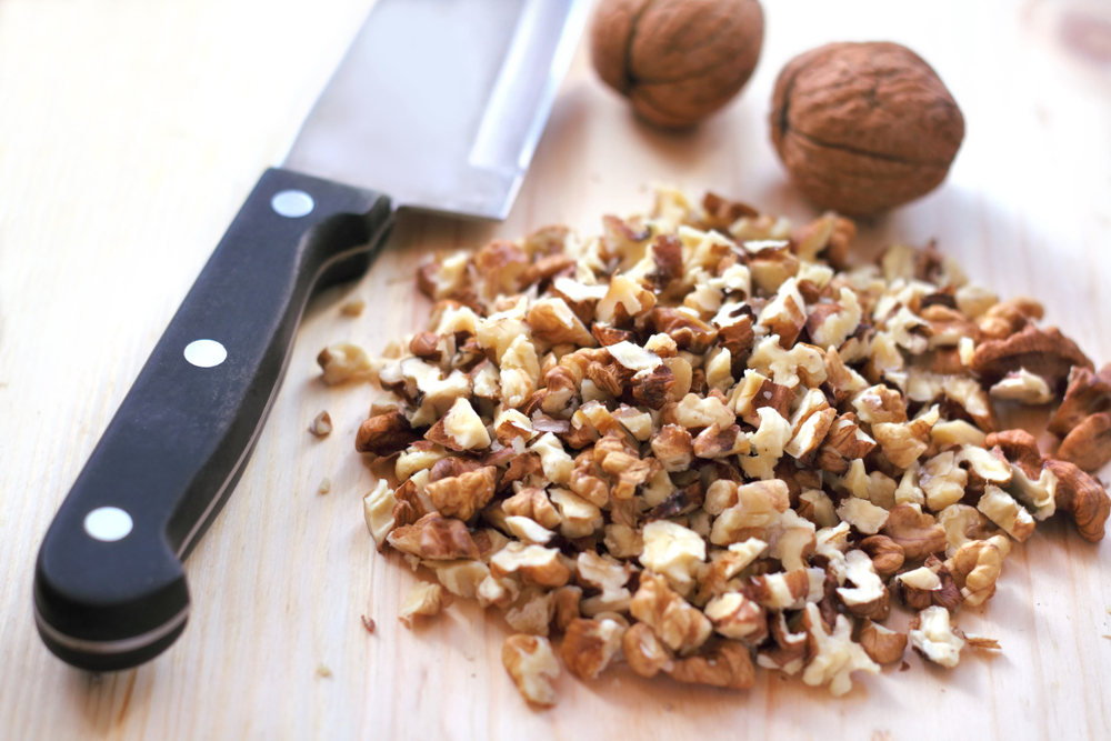 chopped walnuts on a boad with a knife and two whole walnuts. 