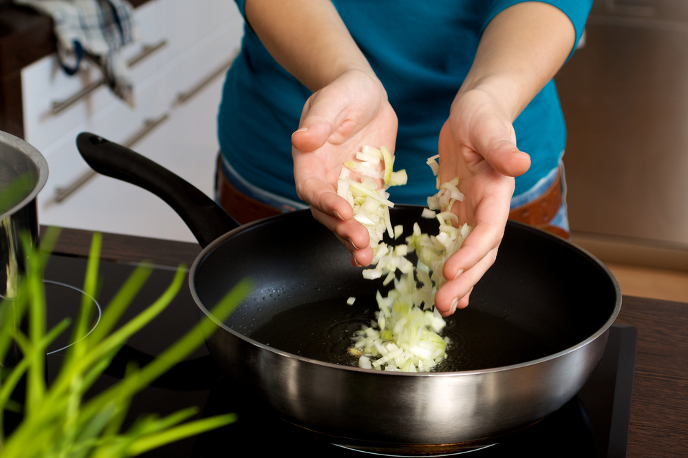 Woman drops onions into a black pan
