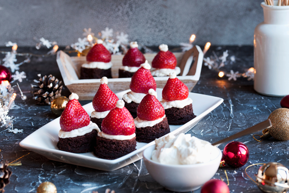 Vegan brownie bites topped with coconut cream and strawberries to look like Santa hats
