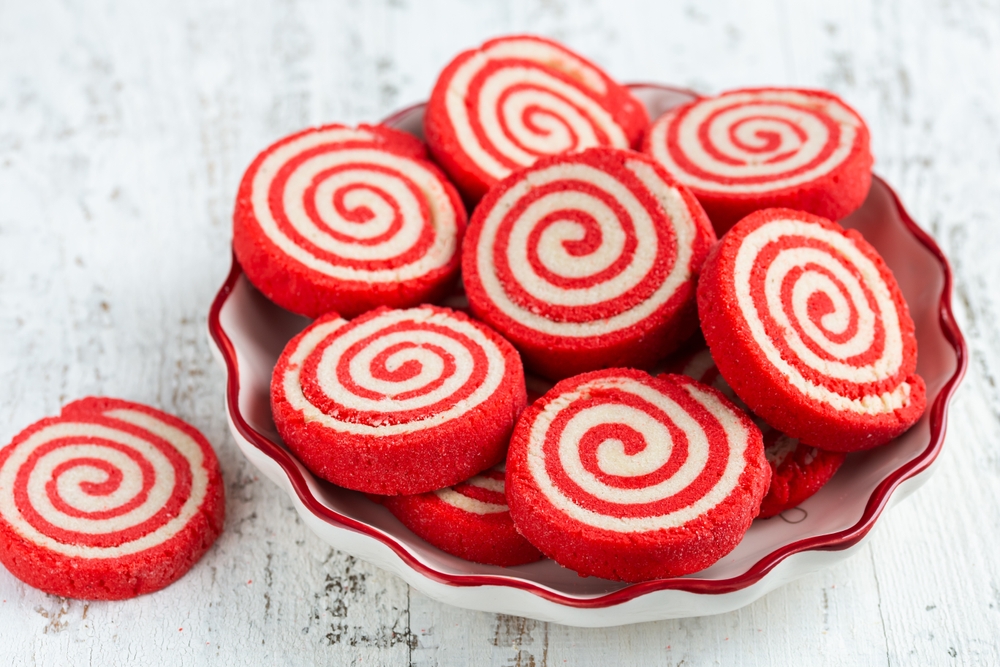 Red sugar pinwheel cookies arranged on a white wooden board