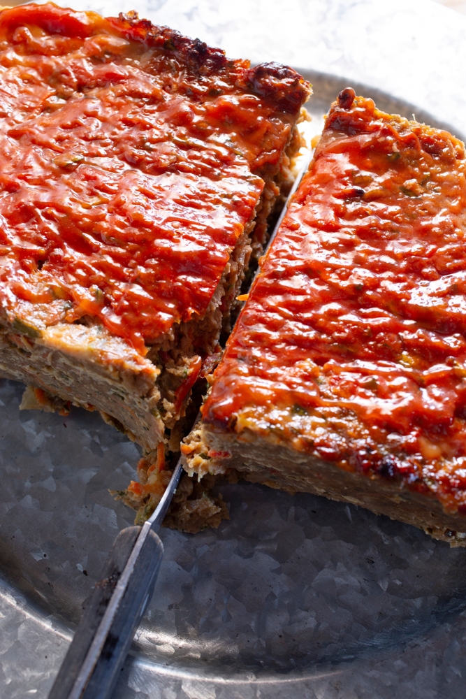 A view of a knife cutting a vegan meatloaf in half.