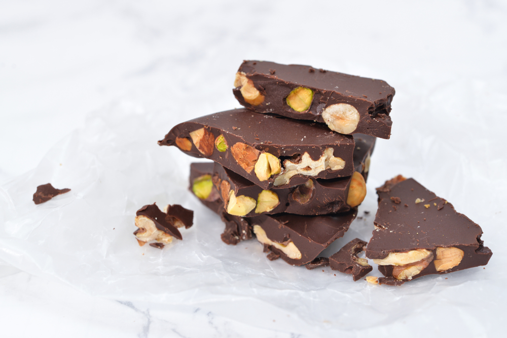 Vegan peppermint bark topped with chopped pistachios and almonds on parchment paper