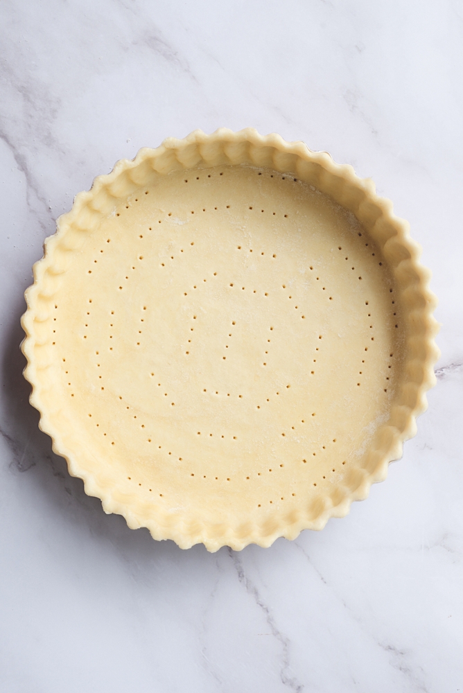 pastry pie dough in pie plate on white marble table preparation for bake.