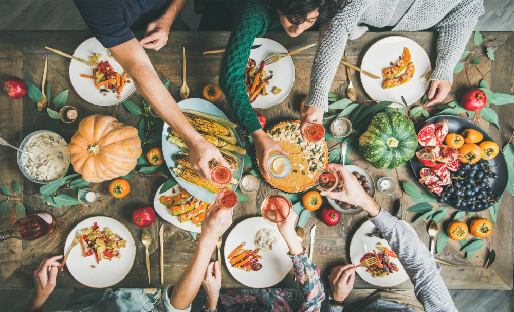 Vegan or vegetarian Thanksgiving, Friendsgiving holiday celebration. Flat-lay of friends eating meals at Thanksgiving Day table with pumpkin pie, roasted vegetables, fruit, rose wine, top view. These vegan Thanksgiving recipes  are perfect 