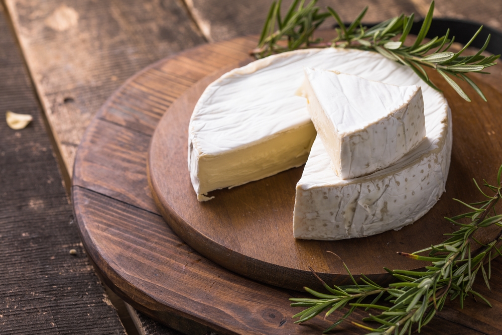 Organic farm camembert or brie cheese on a wooden board with rosemary and nuts, honey.