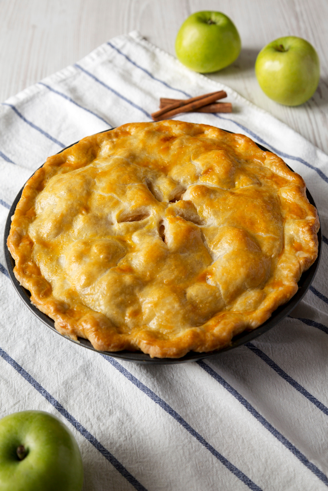 Pie on cloth with some cinnamon sticks and apples. 