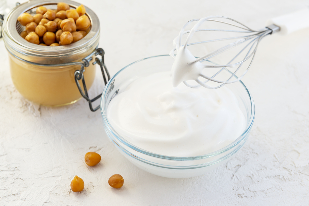 Whipped chickpea aquafaba in a glass bowl on a background of boiled chickpeas. 
