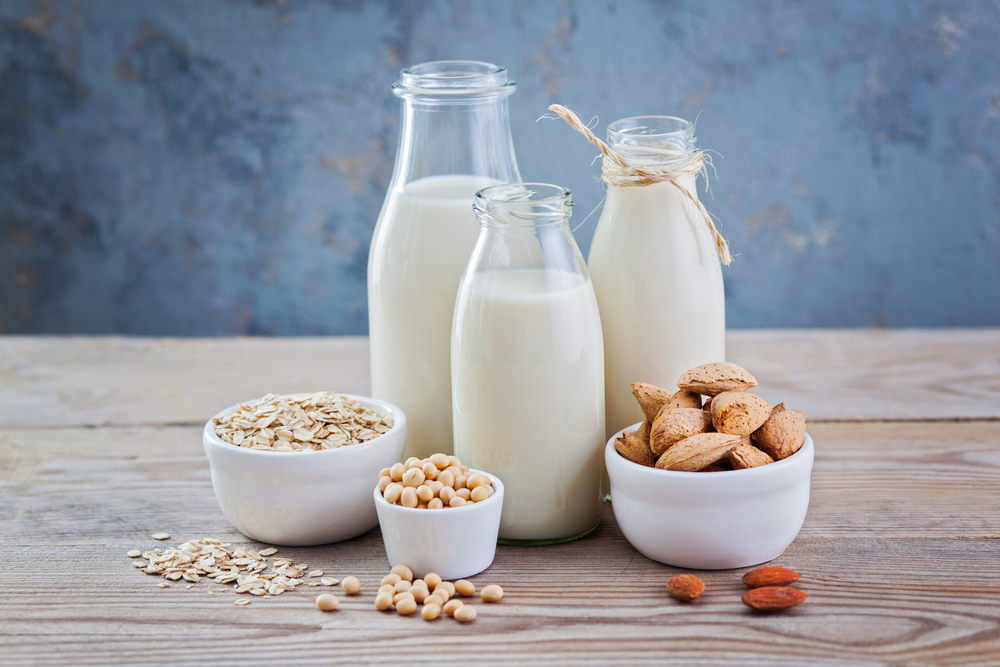 three bottles of dairy-free milk  with nuts and oats around. 