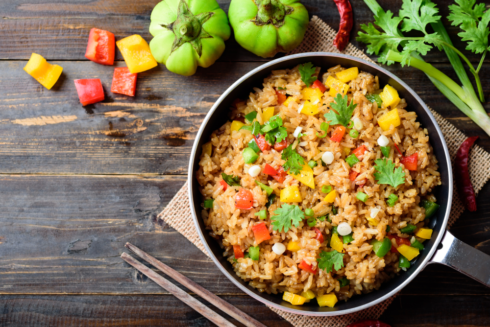 Fried rice with vegetables in cooking pan on wooden table, Asian food, top view