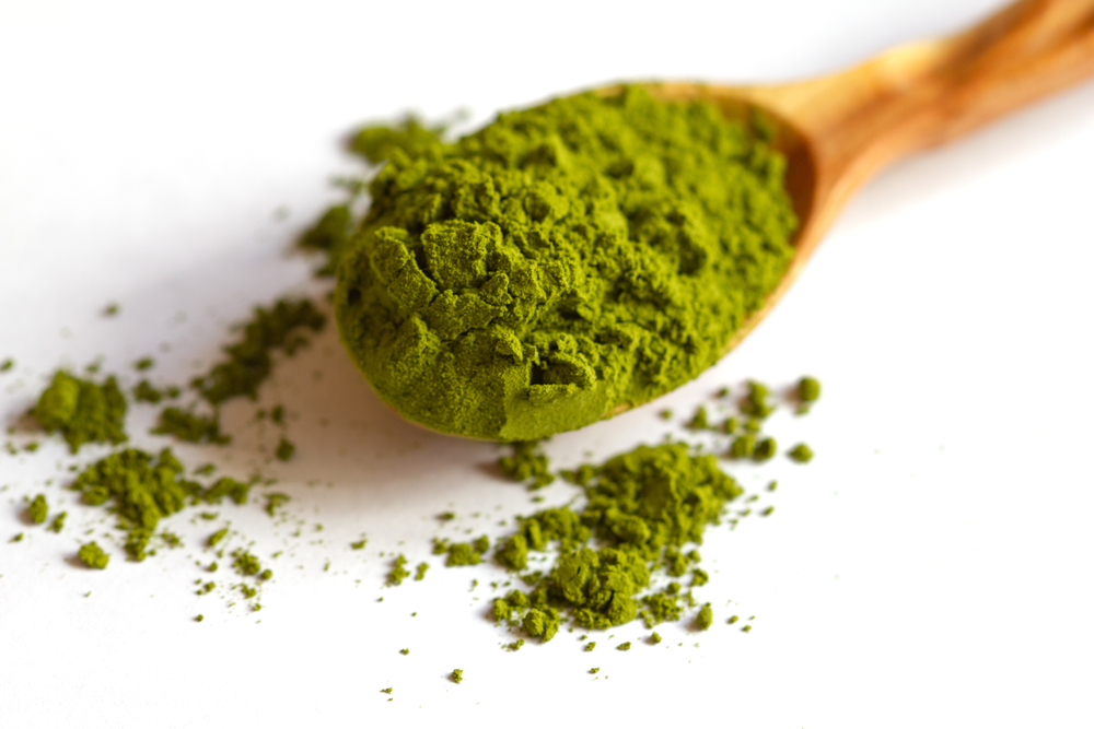 A wooden spoon full of matcha powder, there is matcha powder split on the white surface.  