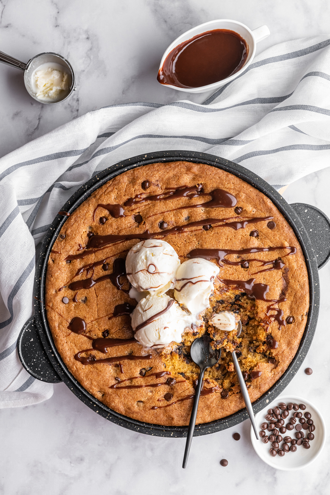 Skillet cookie with scoops of vanilla ice cream on a white marble background with drops of chocolate